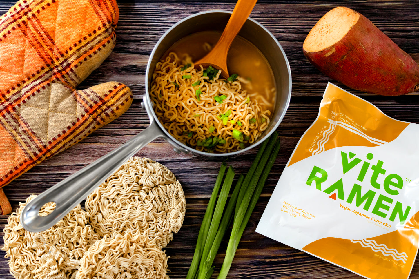 A photo of a pot of cooked Vite Ramen Vegan Japanese curry with fresh ingredients nearby, and a festive fall oven mit.